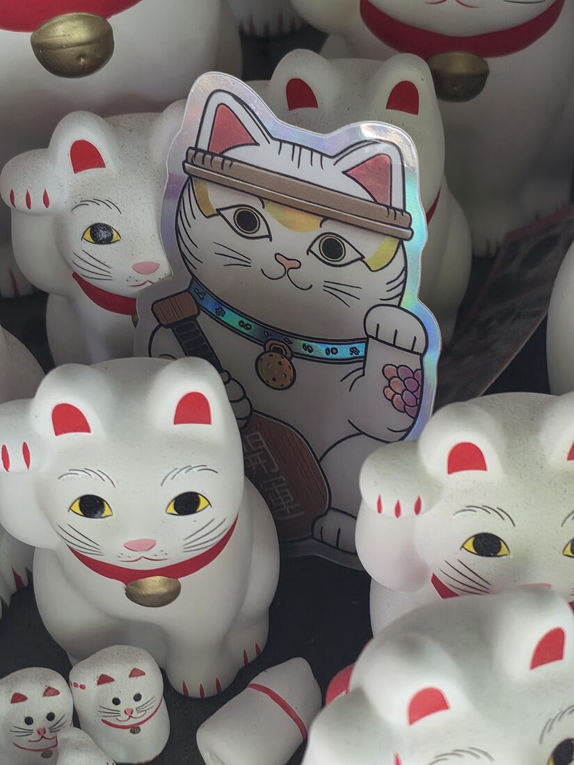 Our Lucky Cat Plays Pickleball sticker among the maneki-neko at Gotokuji
